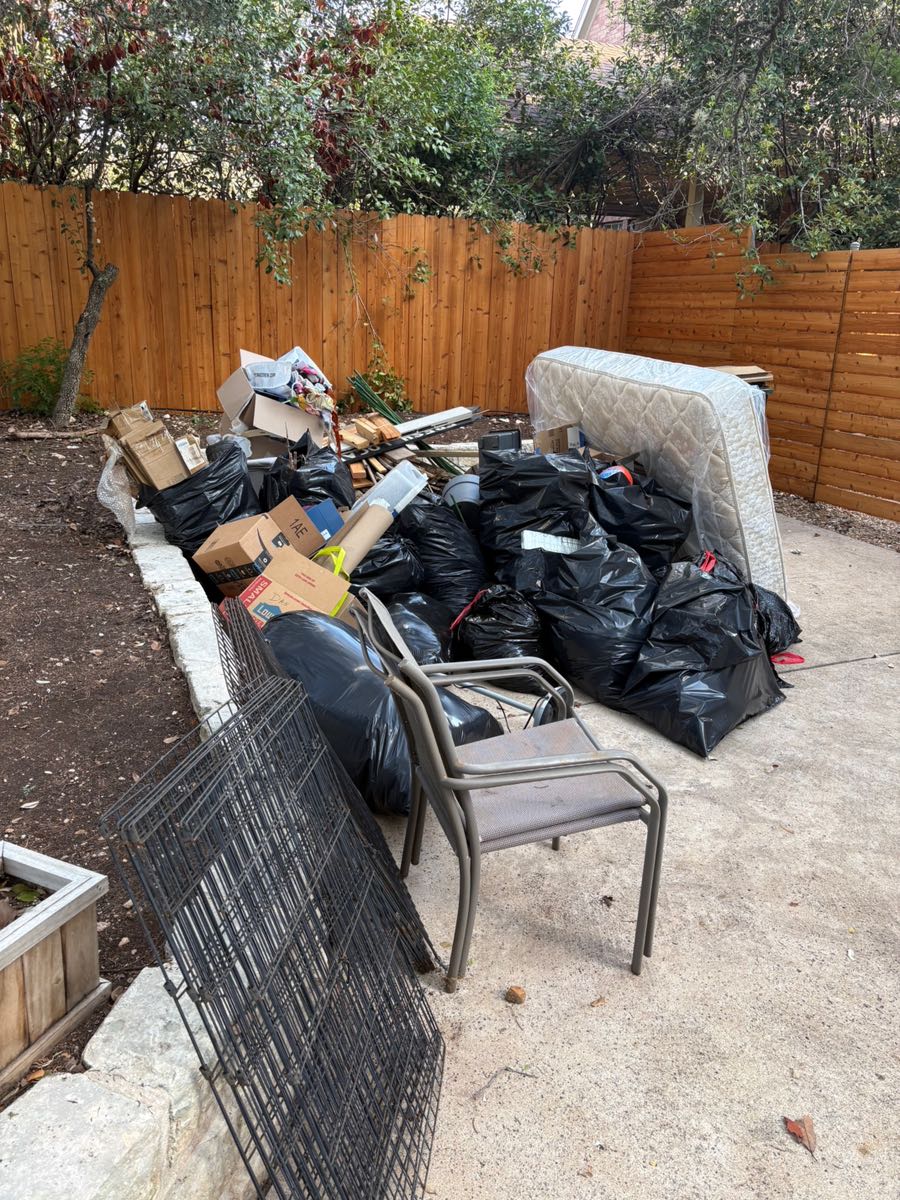 Back patio stacked with bagged trash, a mattress, a patio chair, a dog crate and cardboard before a haul