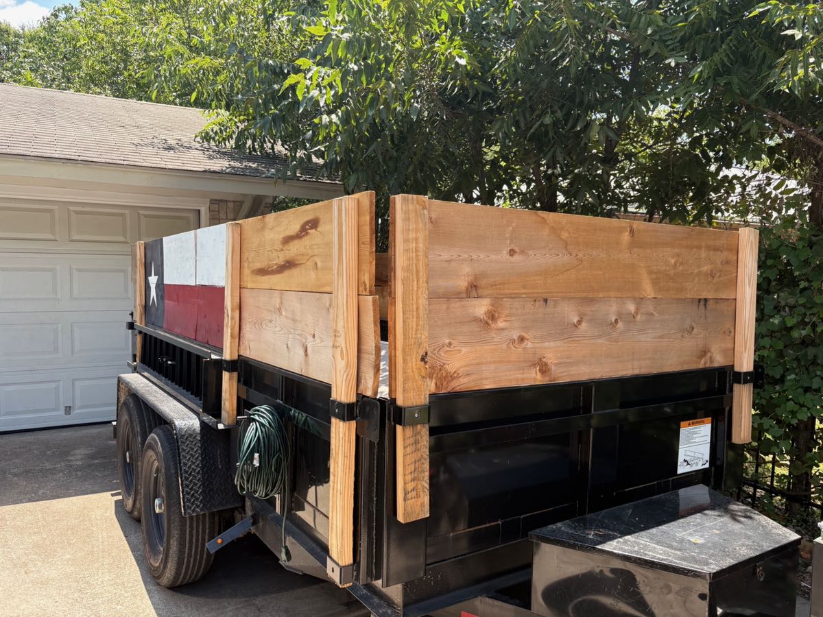 The 12-foot high-wall dump trailer with cedar side extensions and a Texas flag panel, parked on a driveway